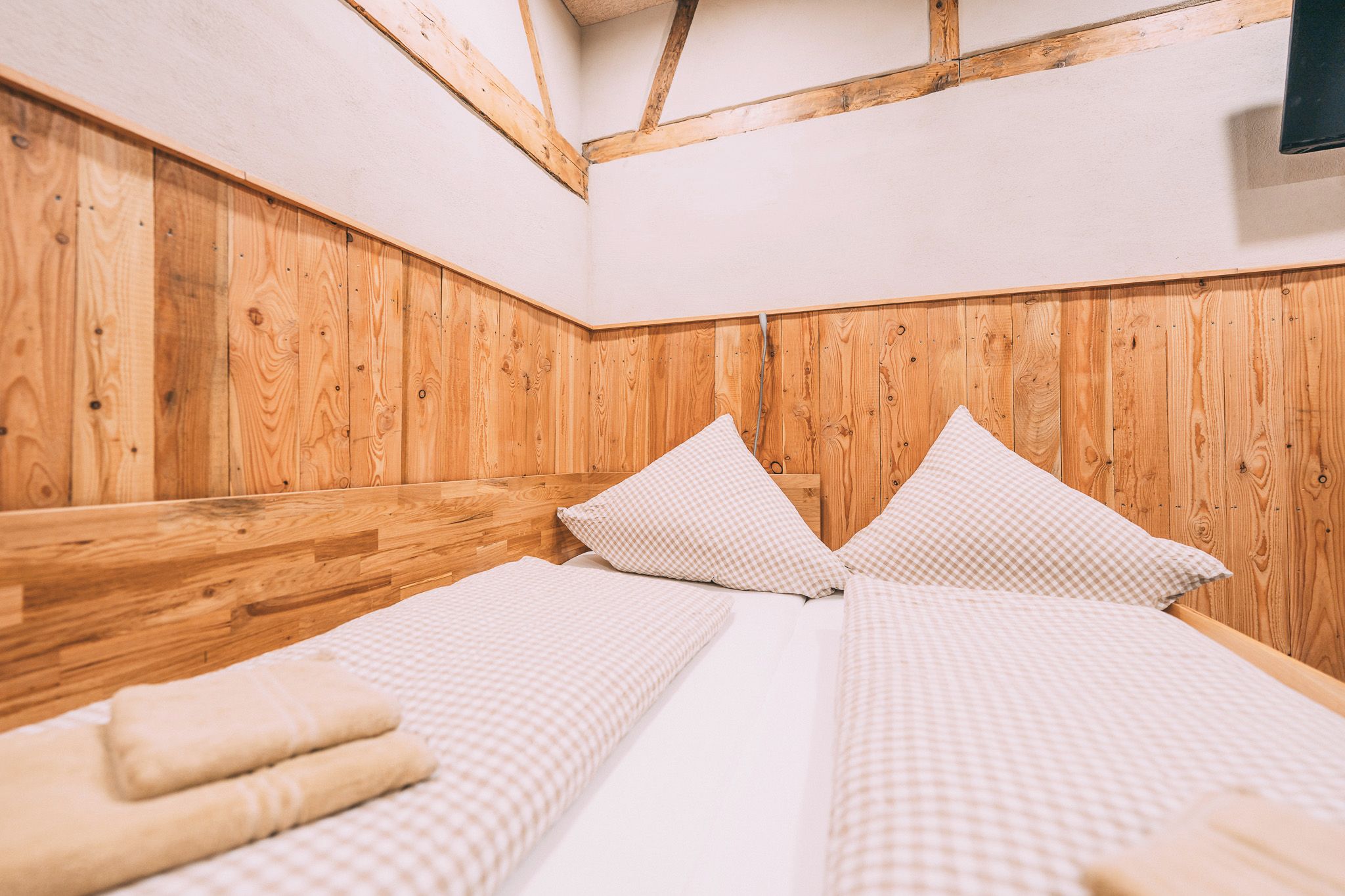 A room with a wooden headboard, two beds with checkered bedding, and a visible cable.