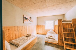 Une petite pièce avec deux lits superposés en bois, une fenêtre donnant sur un paysage agréable et une échelle en bois.
