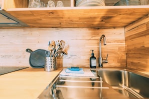 A kitchen with a stainless steel sink, wooden cabinets, and a utensil holder with various kitchen tools. - Möttelin Gut Hügle (Ravensburg)