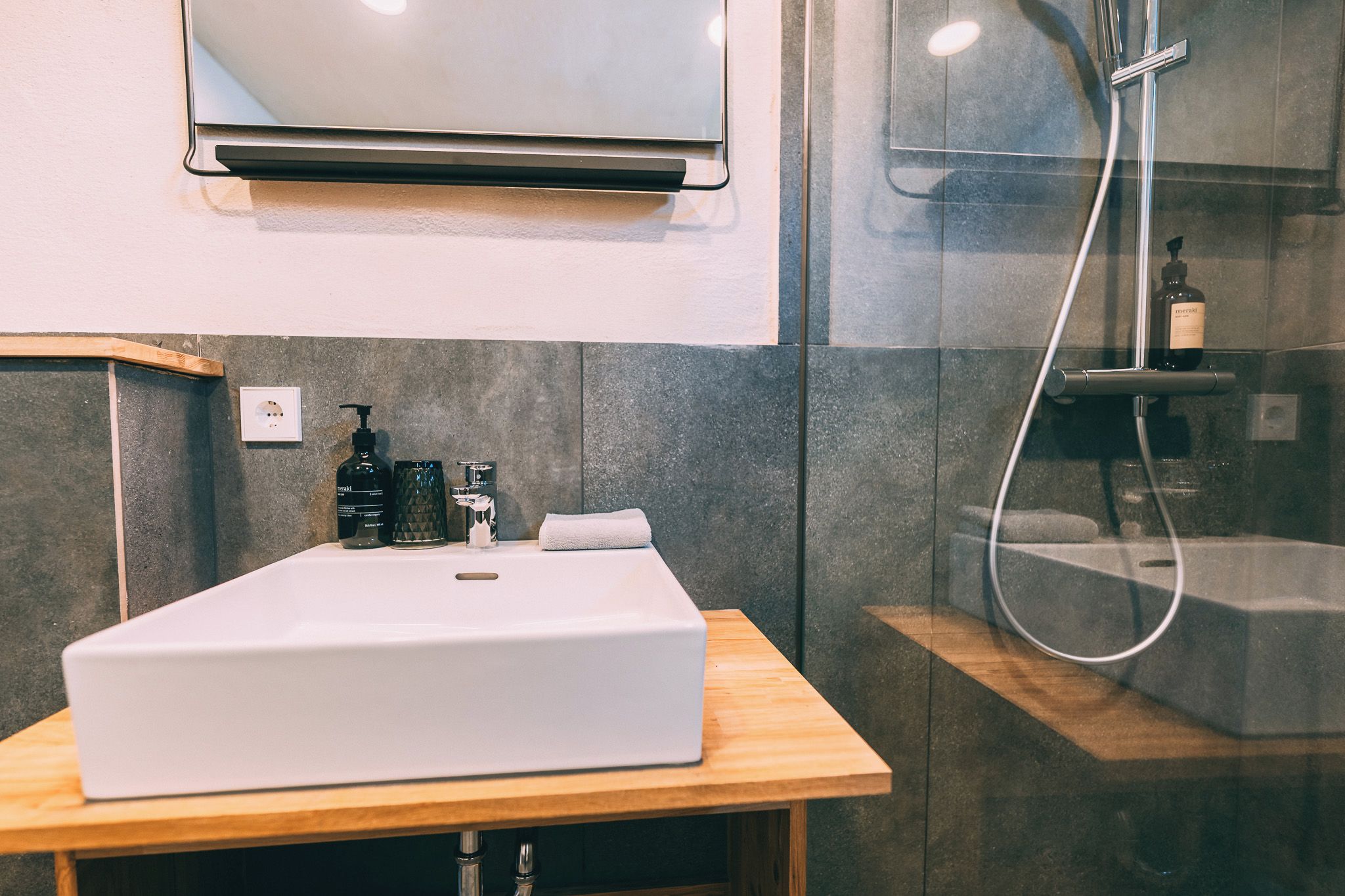 Une salle de bain moderne avec un lavabo blanc, une douchette à main et un miroir au-dessus du lavabo.
