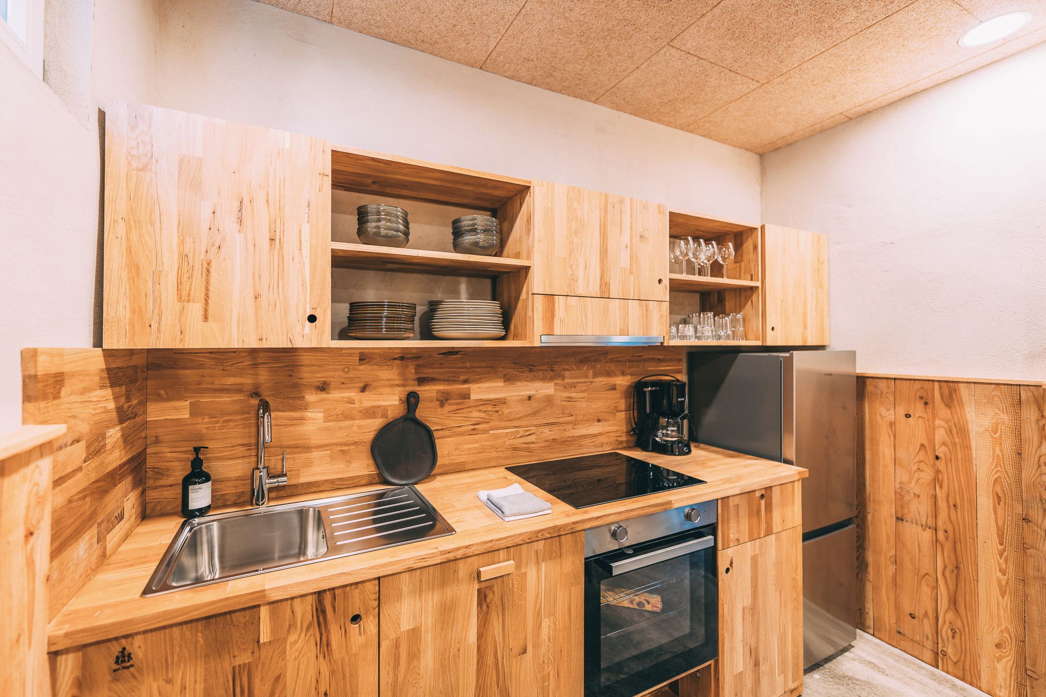 Een keuken met houten kastjes, een RVS spoelbak, een koffiezetapparaat en een inbouwoven.