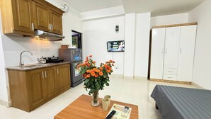 A compact kitchen with wooden cabinets, a refrigerator, and a sink. There's a small table with a vase of flowers and a remote control. - Era Apartment Kham Thien (Hanoi)