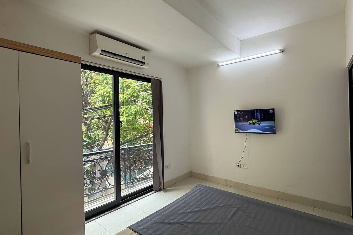 A room with a sliding glass door to a balcony, a flat-screen TV mounted on the wall, and a ceiling-mounted air conditioner.