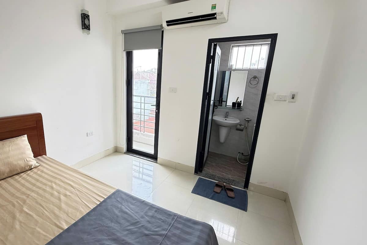 A bedroom with a bed, a bathroom with a sink and mirror, and a door leading to an outdoor area.