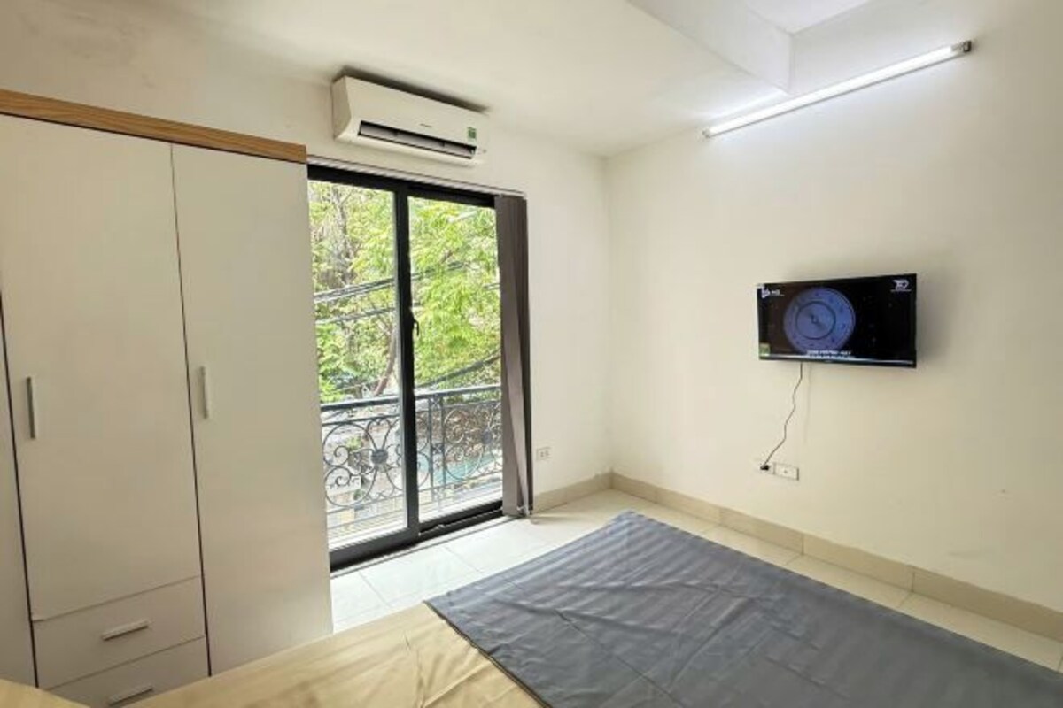 Une chambre dotée d’une porte-fenêtre coulissante donnant sur un balcon, d’un téléviseur à écran plat fixé au mur et d’un lit avec un matelas gris.