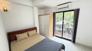 A bedroom with a bed, a wardrobe, an air conditioning unit, and a balcony with a view of greenery. - Era Apartment Kham Thien (Hanoi)
