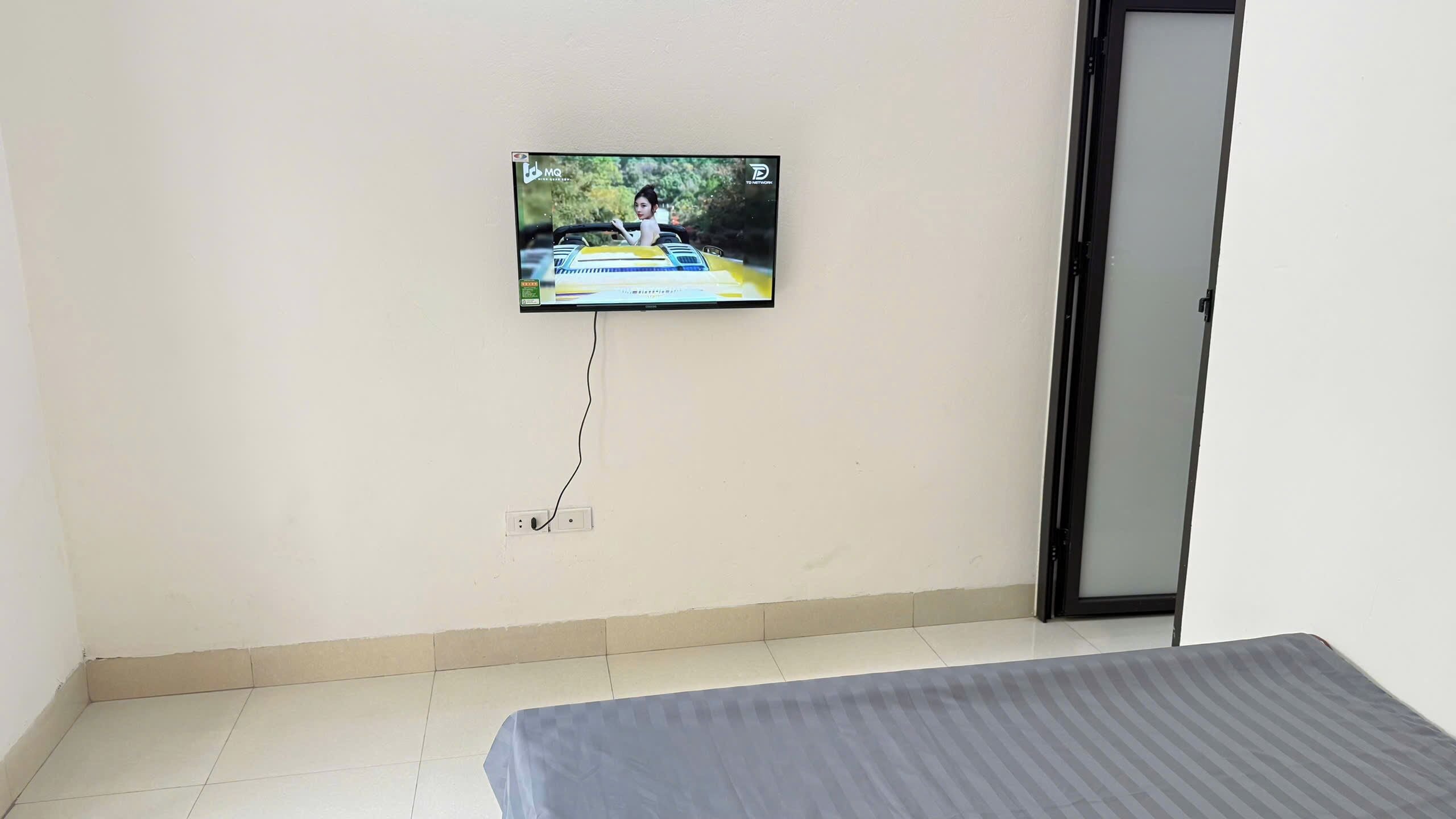 A room with a bed, a wall-mounted TV, and a door.