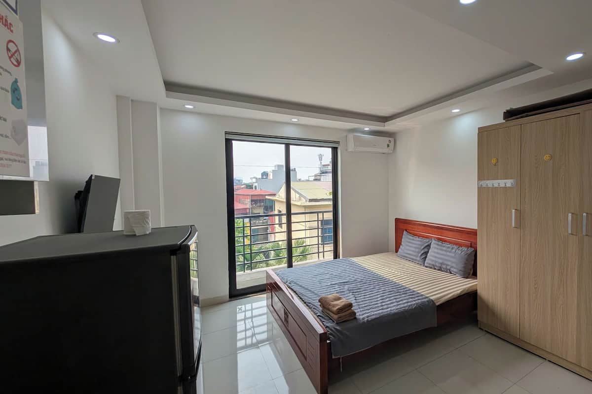 A bedroom with a bed, a wardrobe, a desk, and a window with a city view.