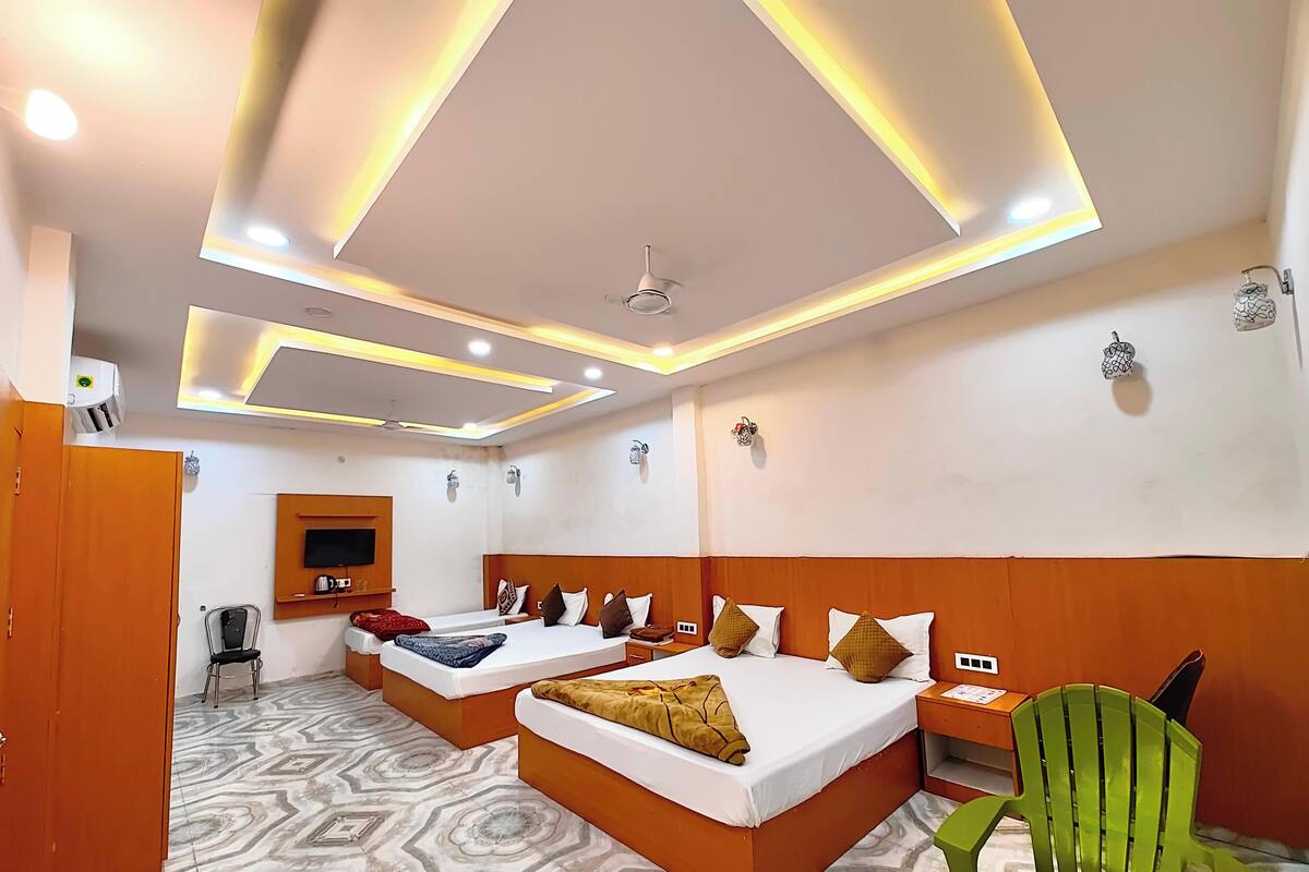 Een hotelkamer met twee bedden, een groene stoel, een televisie en een plafondventilator.