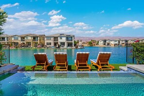 Zona de piscina con tres tumbonas, vista despejada de un complejo residencial y montañas al fondo.