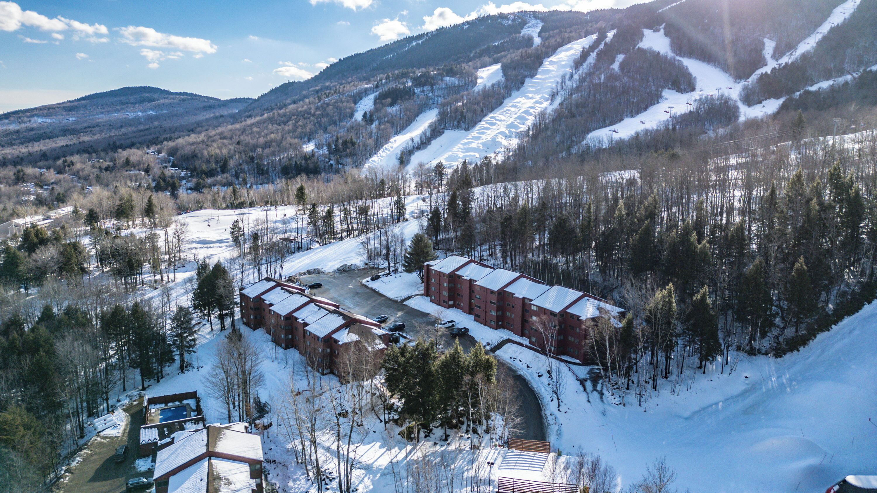 A snow-covered mountainous area with a building complex featuring multiple red brick buildings and a parking area.