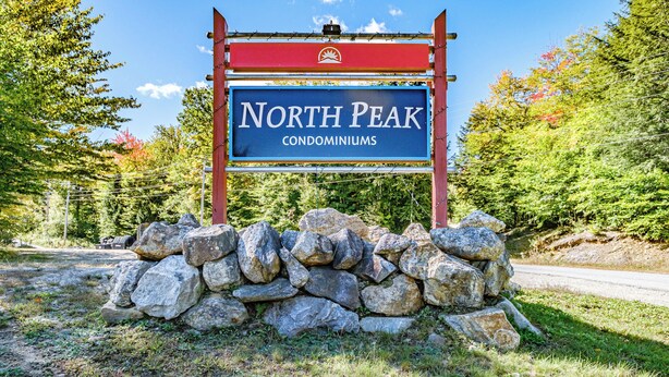 A sign for North Peak Condominiums with a stone wall in front.