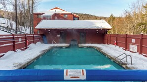 A swimming pool with a blue tarp in the foreground, a red building with a snow-covered roof in the background, and a snowy landscape.