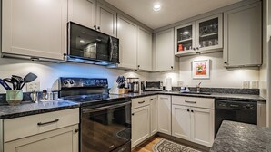 A modern kitchen with white cabinets, a black stove, a microwave, and a dishwasher.
