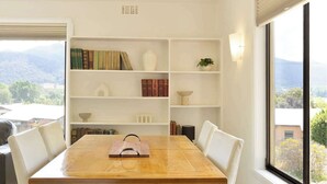 Un comedor con una mesa de madera, sillas blancas y una estantería con libros y adornos.