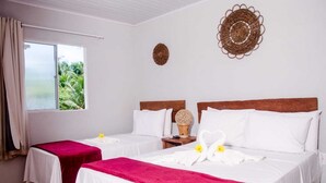 A hotel room with two beds, a window with curtains, a decorative wall hanging, and a small table with a lamp. - CHALES DO TOQUE (São Miguel dos Milagres)