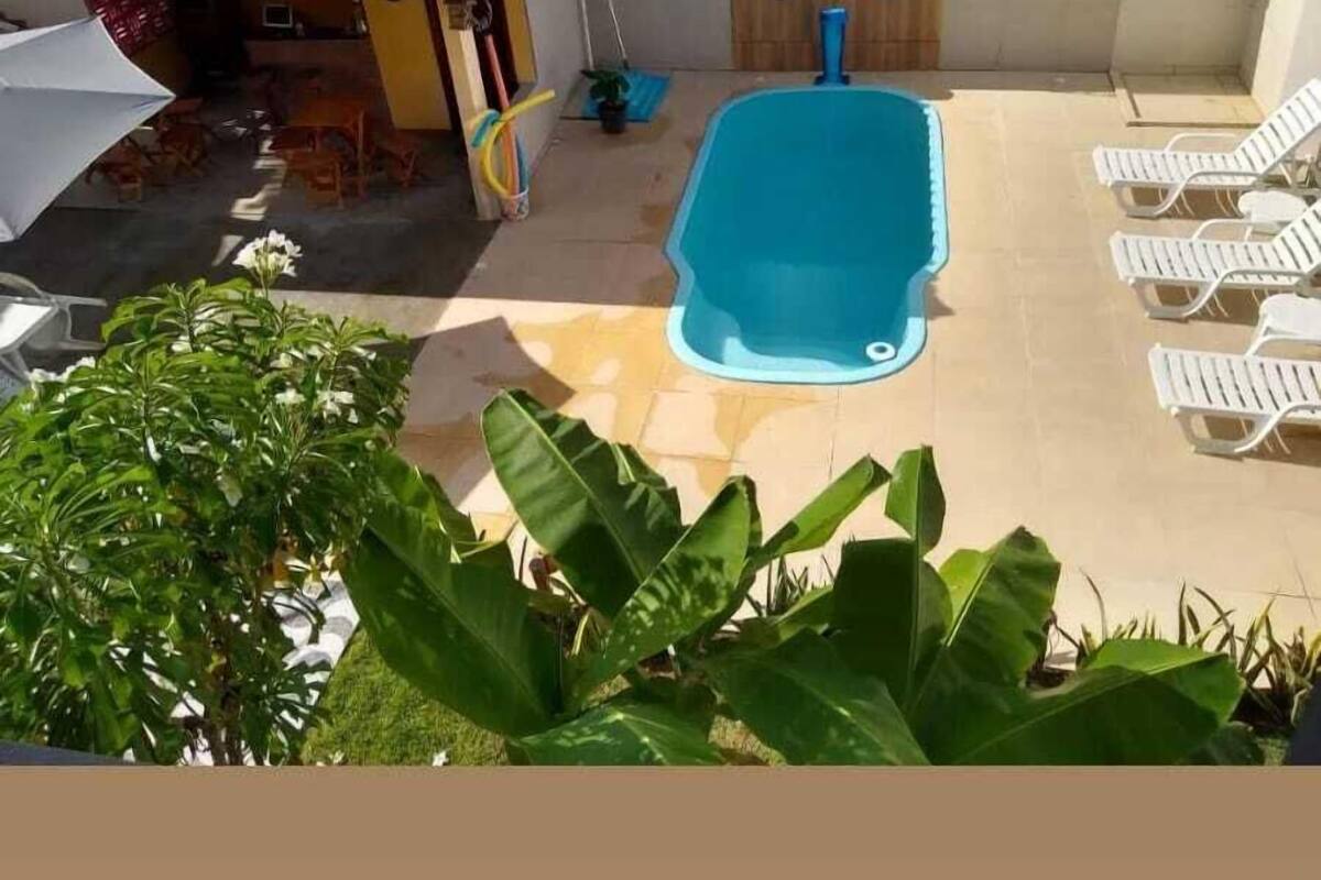 Una piscina con sillas de descanso, un pequeño edificio con techo de tejas y plantas en macetas.