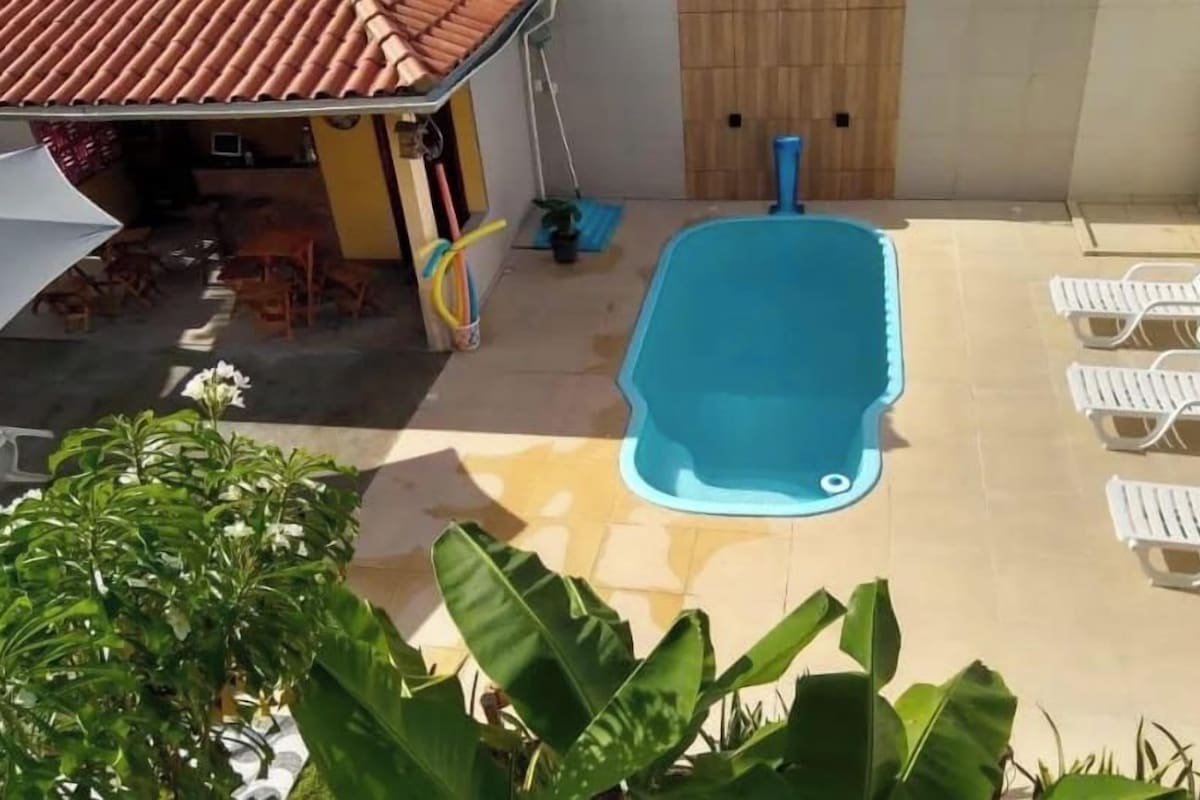 Una piscina con sillas de descanso, un pequeño edificio con techo de tejas y plantas en macetas.