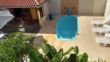 A swimming pool with lounge chairs, a covered patio area, and potted plants.