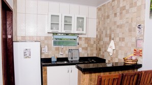 A compact kitchen with white cabinets, a black countertop, a built-in microwave, and a wooden chair. - CHALES DO TOQUE (São Miguel dos Milagres)