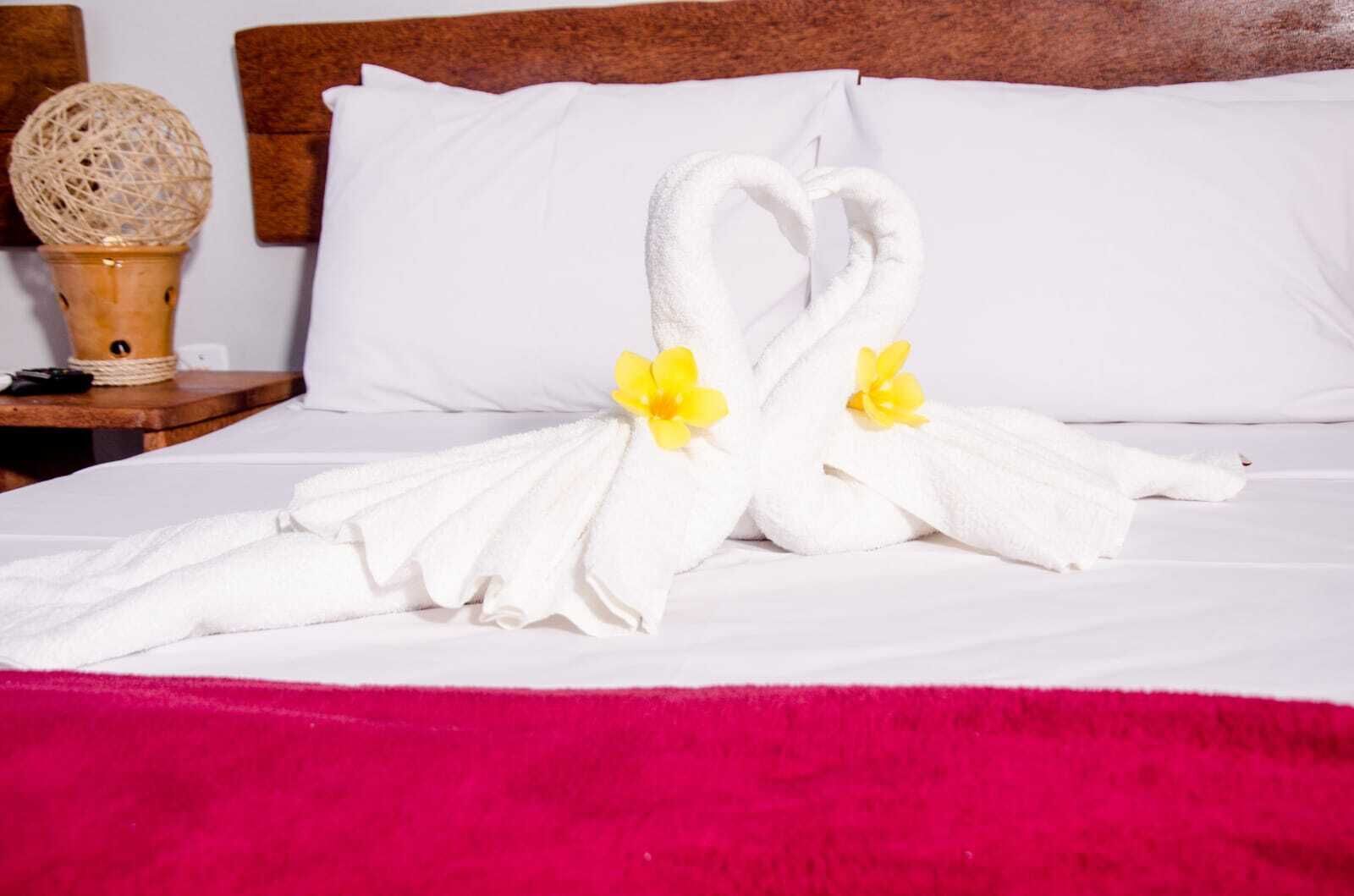 Una cama con sábanas blancas y una colcha rosa, un cabecero de madera y un objeto decorativo en la mesita de noche.