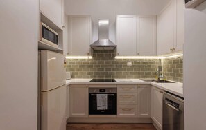 Een compacte keuken met witte kasten, een Bosch oven, een vaatwasser en een magnetron.