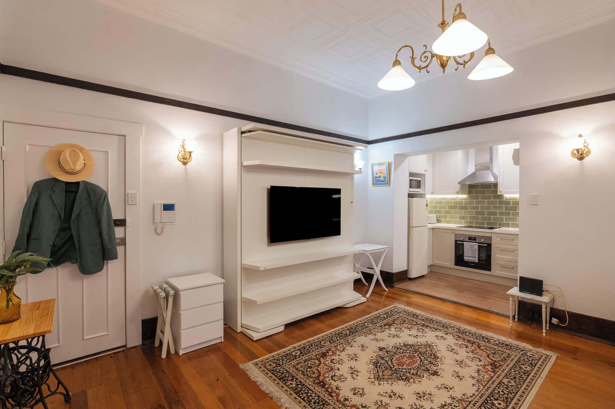 A modern living room with a flat-screen TV, white cabinetry, a dining area, and a kitchen with a tiled backsplash.