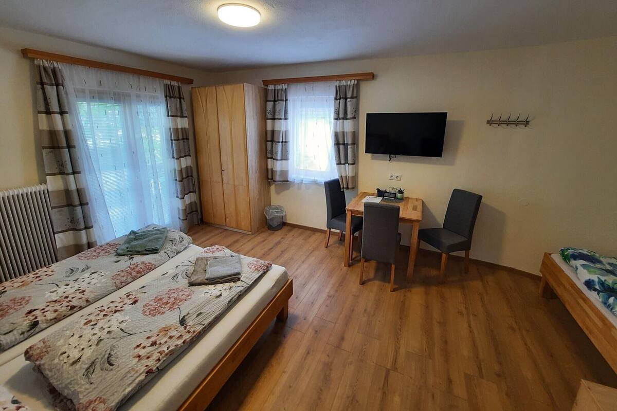 A bedroom with a bed, a desk, two chairs, a TV, and a wardrobe.