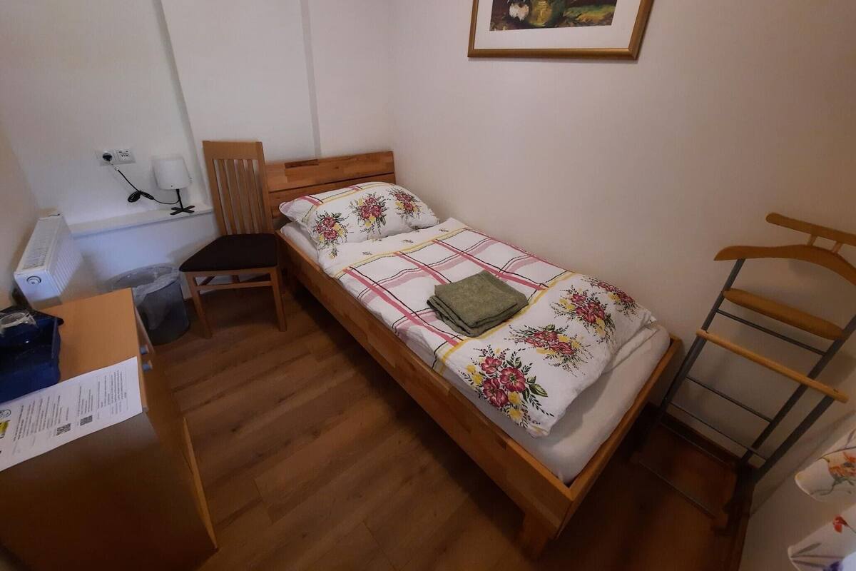 A small, neatly arranged bedroom with a single bed, a chair, a desk, and a radiator.