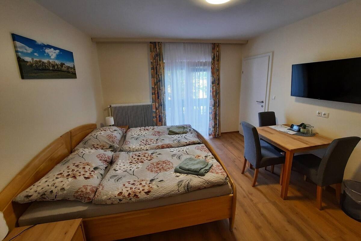 A room with a bed, a desk, a chair, a television, and a radiator.