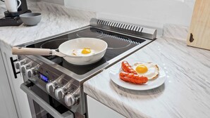 A kitchen with a stovetop, a frying pan with eggs, and a plate with a cooked sausage and egg. - Spacious studio unit in the heart of the Highlands (Louisville)