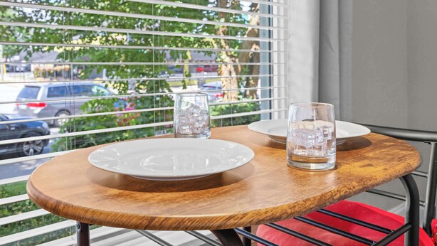 A wooden table with two white plates and two glasses of water, set against a window with blinds. - Spacious studio unit in the heart of the Highlands (Louisville)