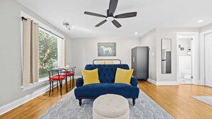 A modern living room with a blue sofa, a round ottoman, and a ceiling fan. - Spacious studio unit in the heart of the Highlands (Louisville)