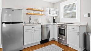A modern kitchen with white cabinets, stainless steel appliances, and wooden shelves. - Spacious studio unit in the heart of the Highlands (Louisville)