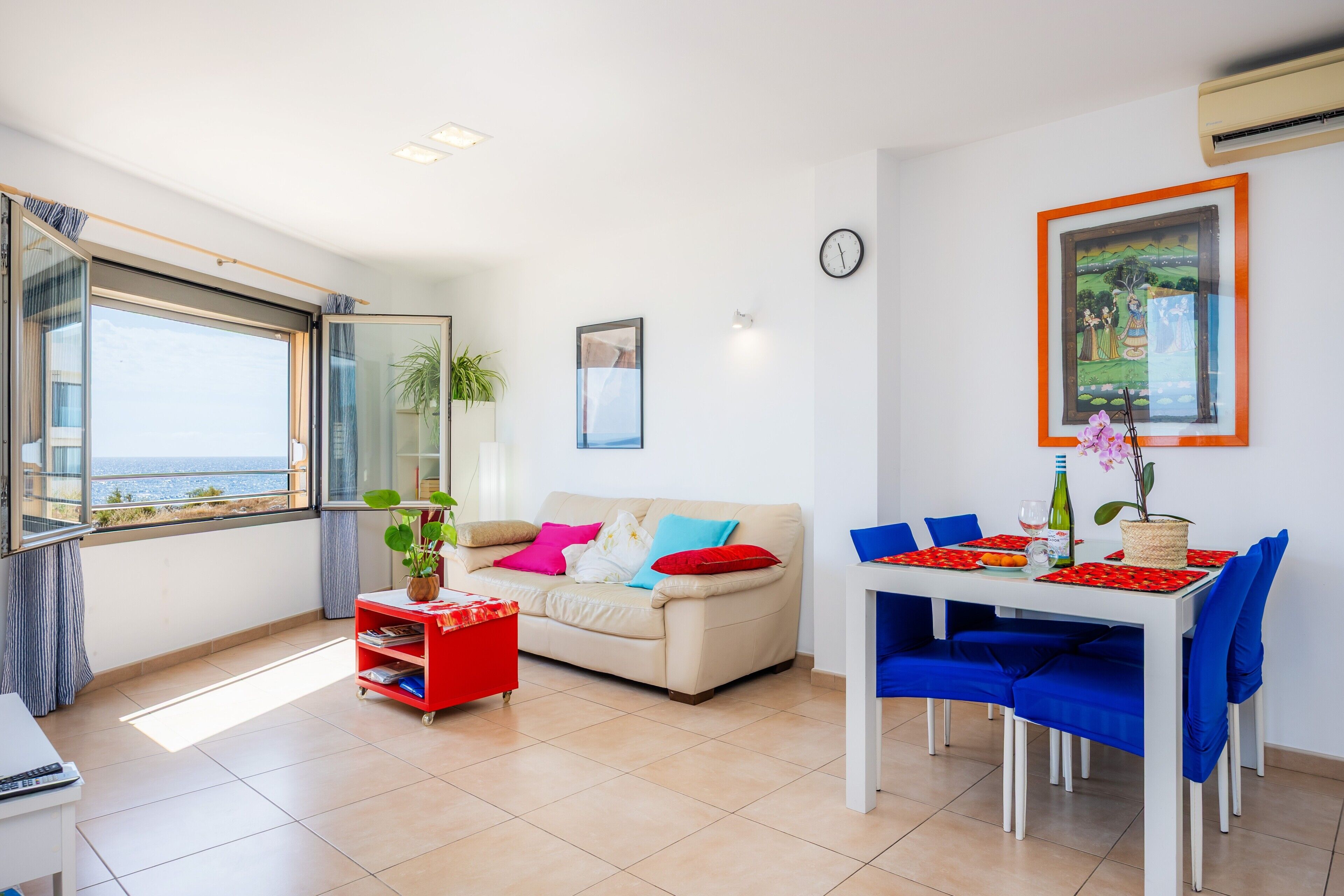 Una sala moderna con un sofá, una mesa de comedor con sillas, una estantería y un ventanal con vistas.