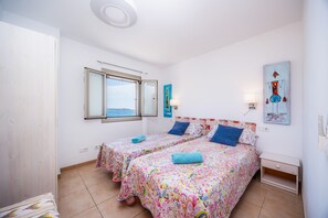 A bedroom with two beds, a window, a nightstand, and a painting.