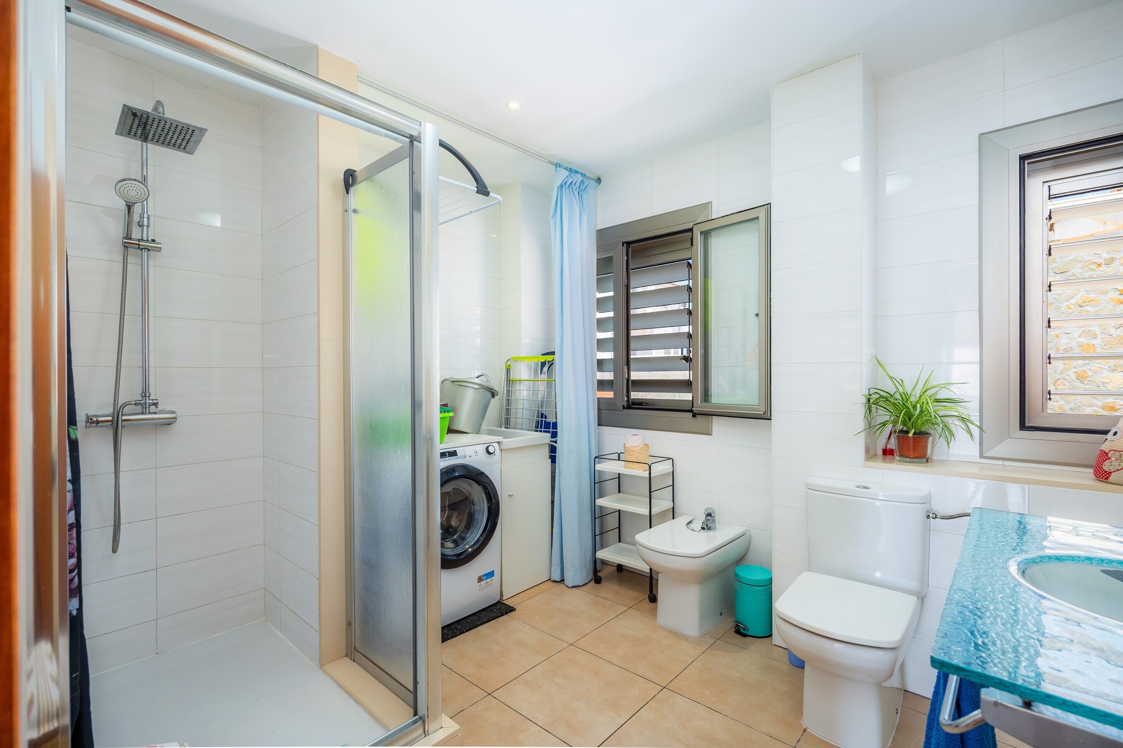 Un baño pequeño con ducha, inodoro, lavabo y lavadora.