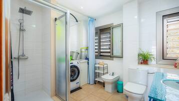 Un baño pequeño con ducha, inodoro, lavabo y lavadora.