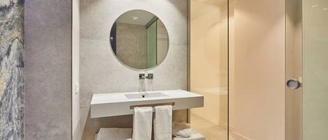 Un baño moderno con pared de mármol, un espejo grande, un lavabo blanco y una cabina de ducha de vidrio.