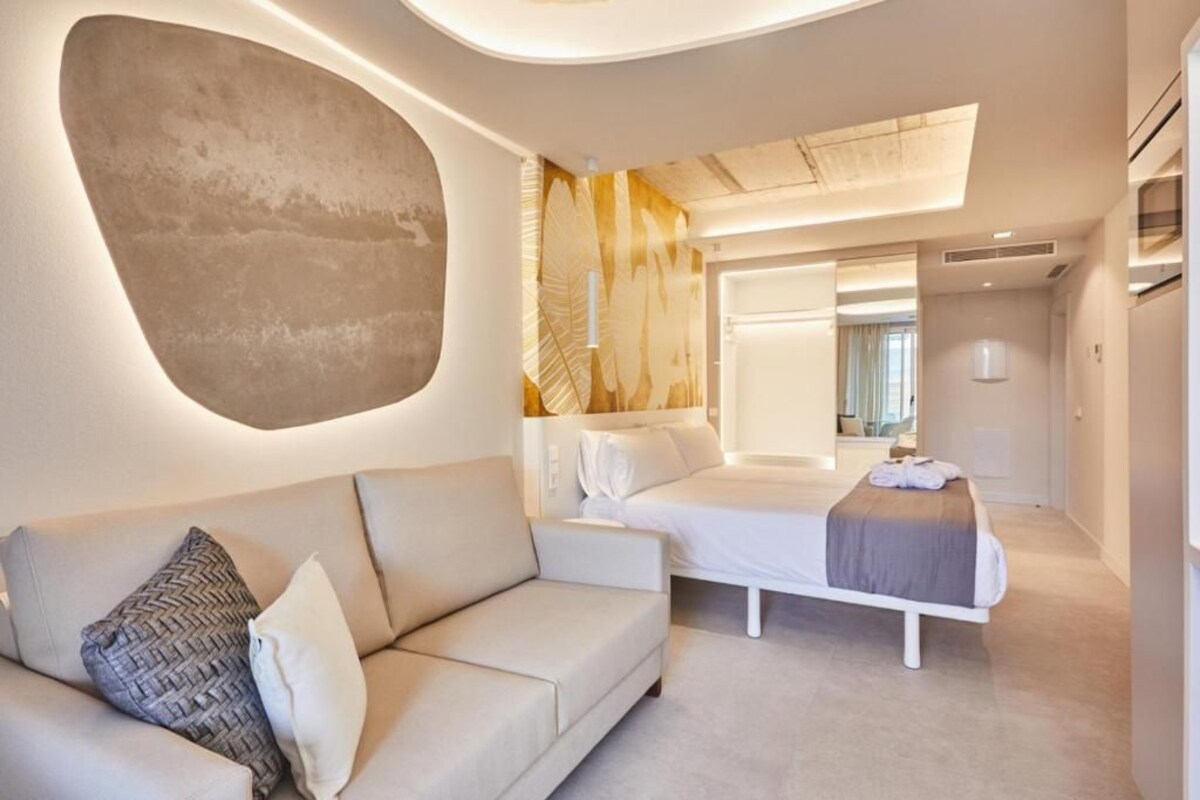 A modern hotel room with a sofa, a bed, and a large abstract wall art piece.