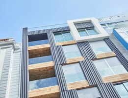 Un edificio moderno con una fachada que combina elementos de madera y metal, grandes ventanales y un cielo despejado.