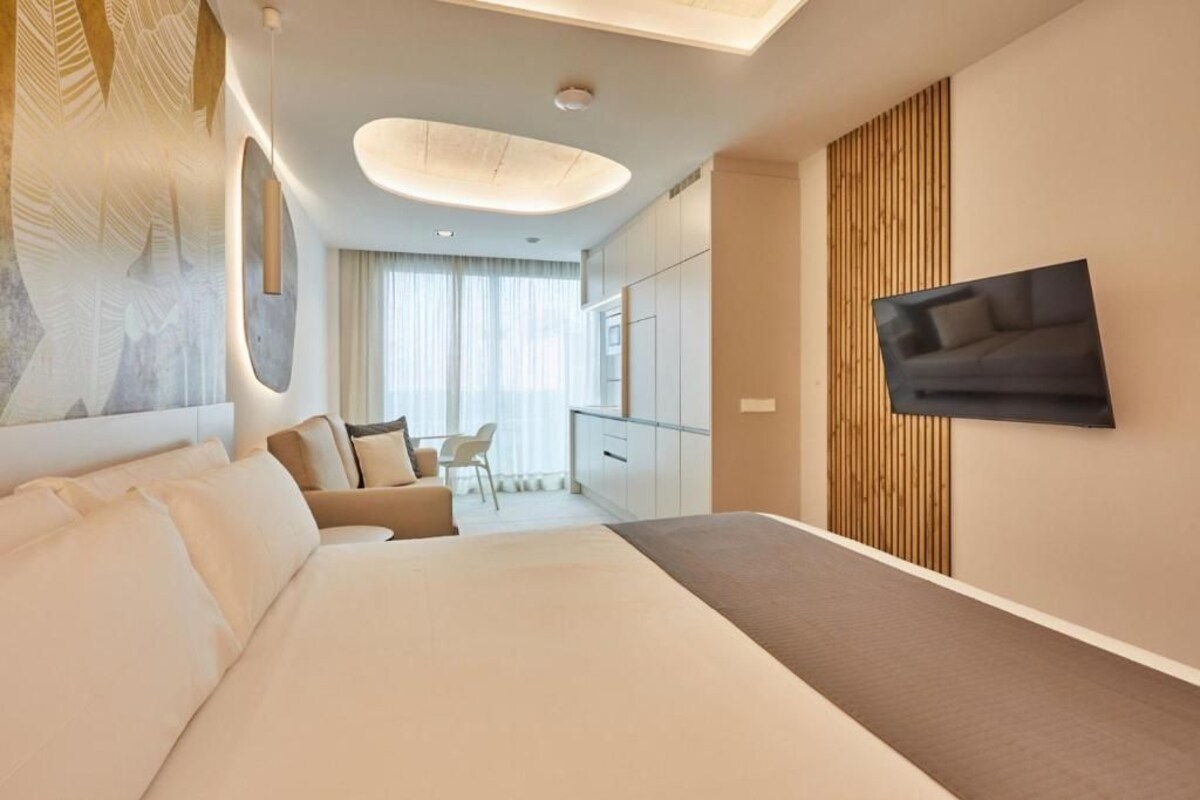 Une chambre d’hôtel moderne avec un grand lit, un téléviseur fixé au mur, un bureau et une chaise.