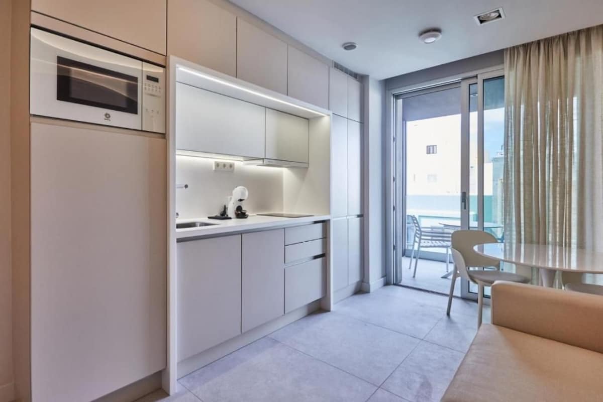 A modern kitchen with a microwave, oven, and sink. There is a balcony with a table and chairs.