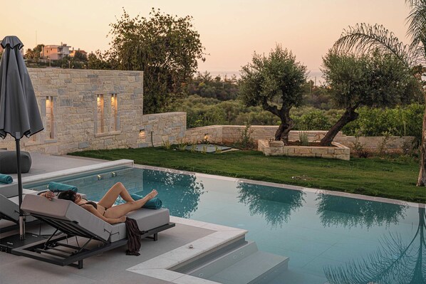 A poolside area with lounge chairs and a stone wall with lights.