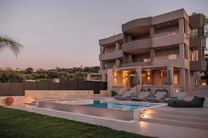 A modern multi-story building with a swimming pool, outdoor seating, and a stone wall.