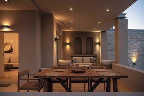 An outdoor dining area with a wooden table and chairs, a sofa, and a stone wall.