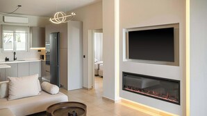 Uma sala de estar moderna com lareira, um sofá, uma mesa de centro e uma área de cozinha com geladeira e uma TV de tela plana.