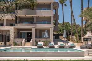 A multi-story building with a swimming pool, outdoor seating, and palm trees. - Kymélia Ground Suite With Private Pool & SeaView (Galatas)