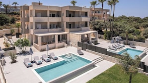 A modern multi-story building with a swimming pool, sun loungers, and a landscaped patio area. - Kymélia Ground Suite With Private Pool & SeaView (Galatas)