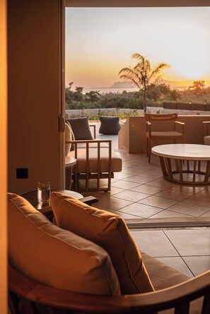 A modern outdoor seating area with a round table and chairs, a glass of water, and a view of the sunset over a body of water. - Kymélia Ground Suite With Private Pool & SeaView (Galatas)